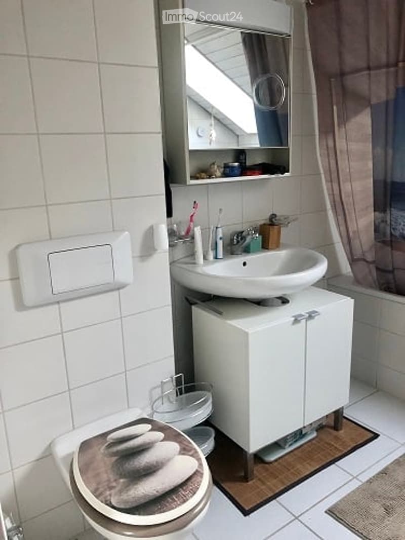 Modern bathroom with white tiles, a floating sink cabinet, a toilet with a decorative seat cover, and a mirror above the sink.