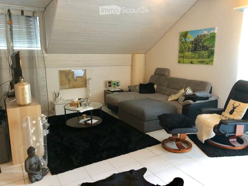 Modern living room with a grey sectional sofa, coffee table, armchair, ottoman, floor lamp, TV, and decorative items including a vase and picture frame.