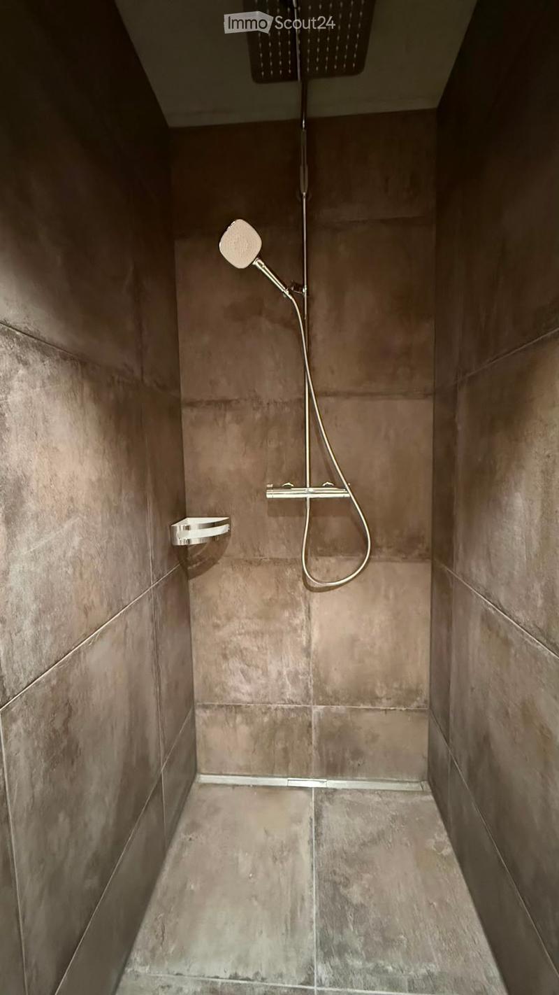 Modern shower area with grey tiled walls and floor, featuring a handheld showerhead, a fixed showerhead, and a chrome tray.