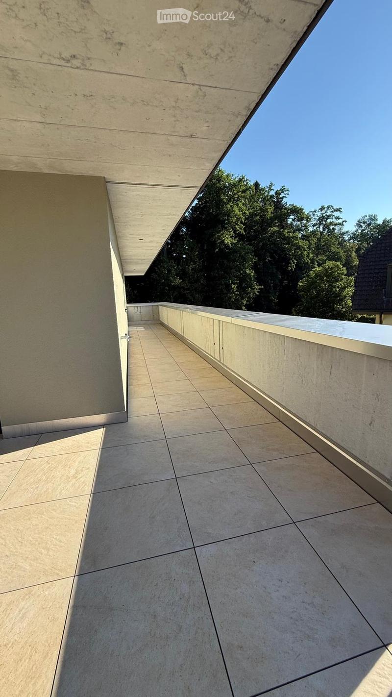 Modern concrete balcony with tiled floor, low wall, and clear sky view.