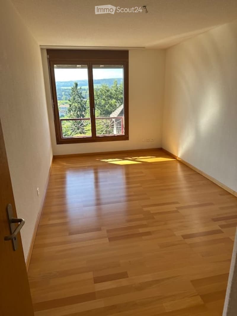 Empty room with wooden flooring and large window offering a scenic view of trees and landscape.