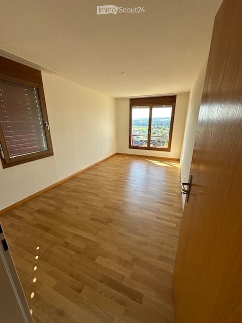 Empty room with wooden flooring, large windows offering a scenic view, and neutral-colored walls.