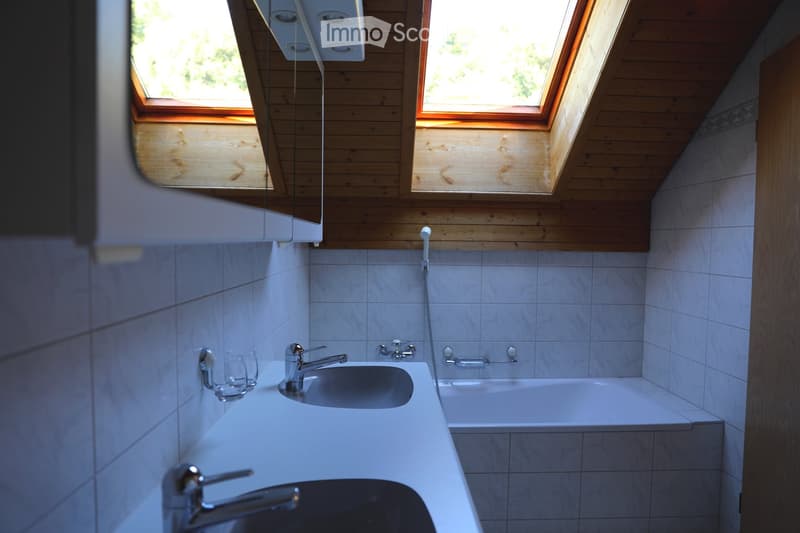 Modern bathroom with white tiles, a sink, a bathtub, and skylight windows providing natural light.
