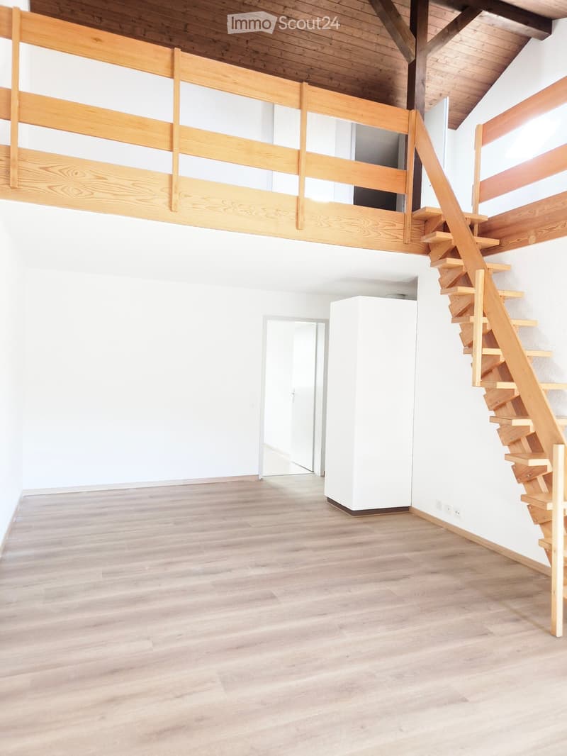 Empty room with light wooden flooring, white walls, a staircase leading to an upper level, and a white column in the center.