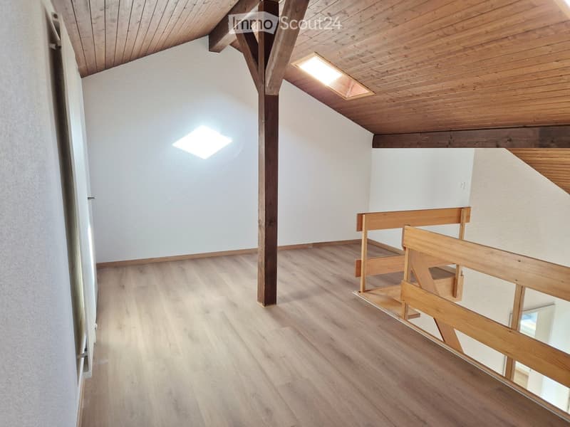 Empty room with wooden flooring, white walls, exposed wooden beams, and a small wooden bench near the corner.