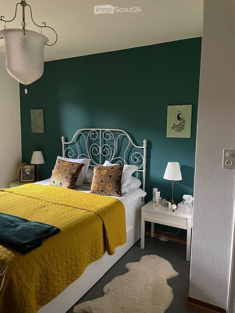 Cozy bedroom with a double bed, yellow quilt, decorative pillows, nightstand with lamp, and a white fur rug on the floor.