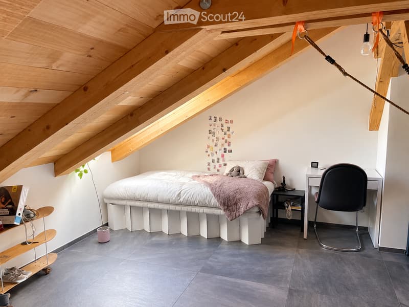 Cozy attic bedroom with exposed wooden beams, skylight, grey tiled floor, white bed with pink blanket, small desk, chair, skateboard, and nightstand.