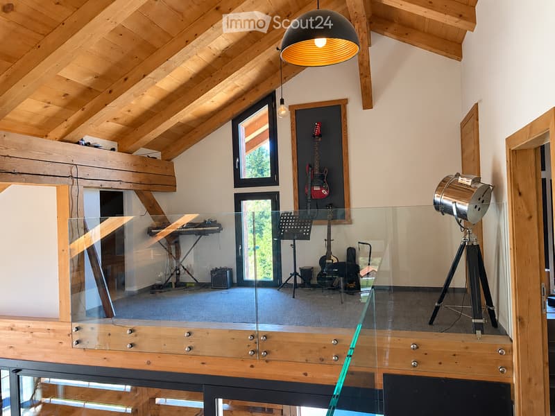 Modern, open-concept room with wooden beams, glass railing, and musical instruments including guitars and a piano.