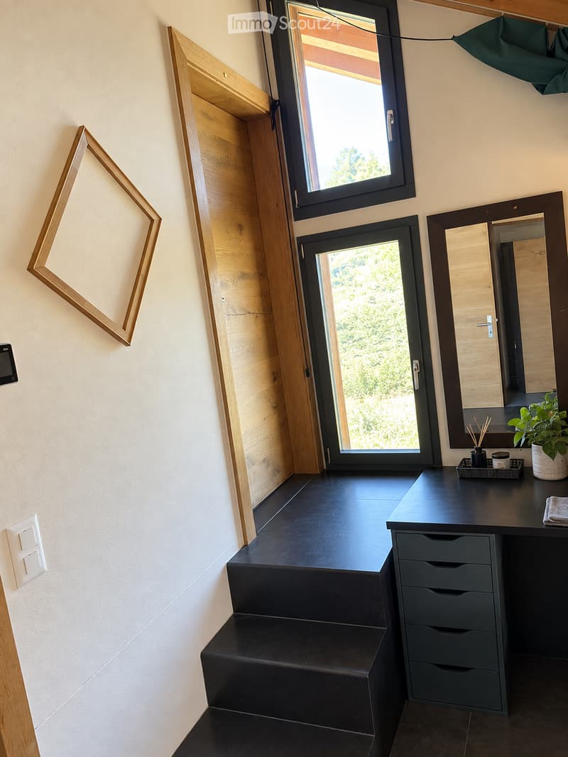 Modern bathroom with dark vanity, mirror, drawer unit, and small plant on the counter. Features large windows and wooden paneling.