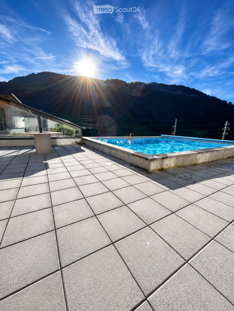 Outdoor area with a swimming pool, tiled floor, and a scenic mountain view in the background.