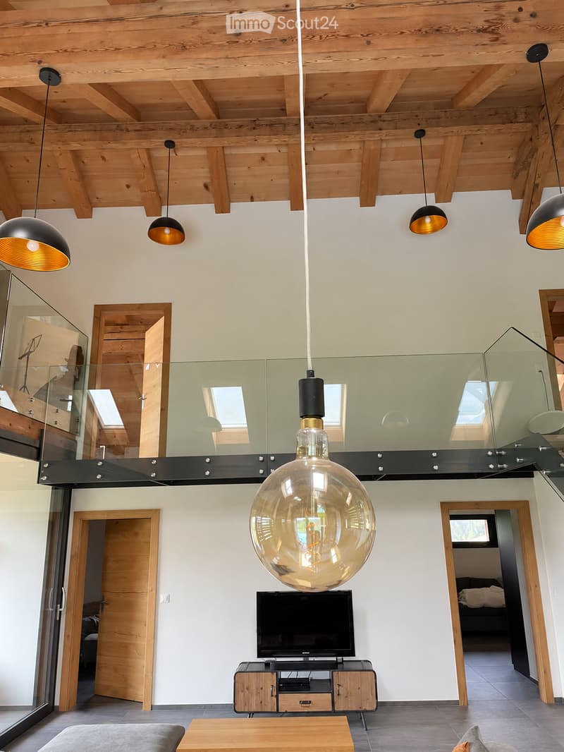 Modern living room with exposed wooden beams, pendant lights, a sofa, coffee table, TV, and TV stand.