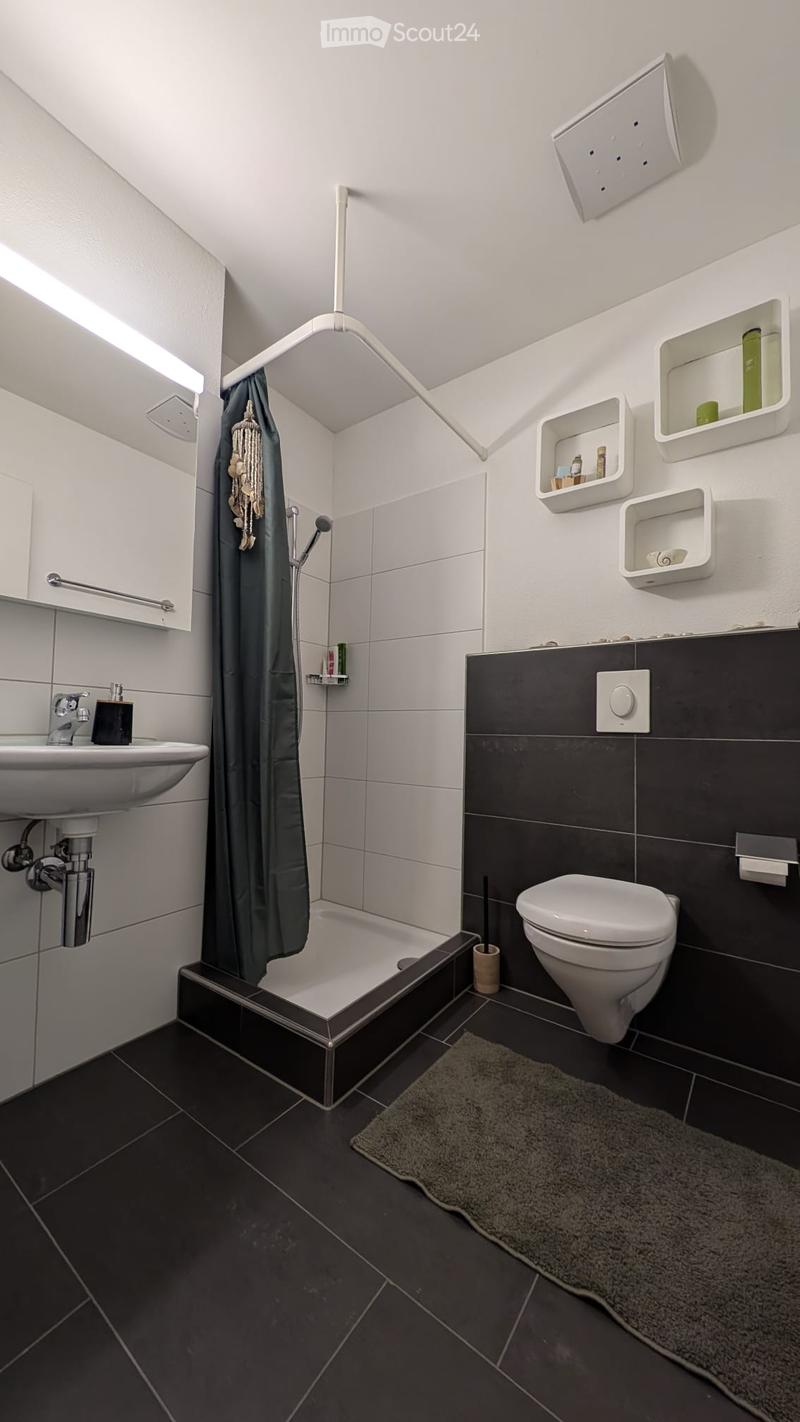 Modern bathroom with dark tiled floor and walls, white bathtub, sink, toilet, built-in shelves, and a shower area with a curtain.