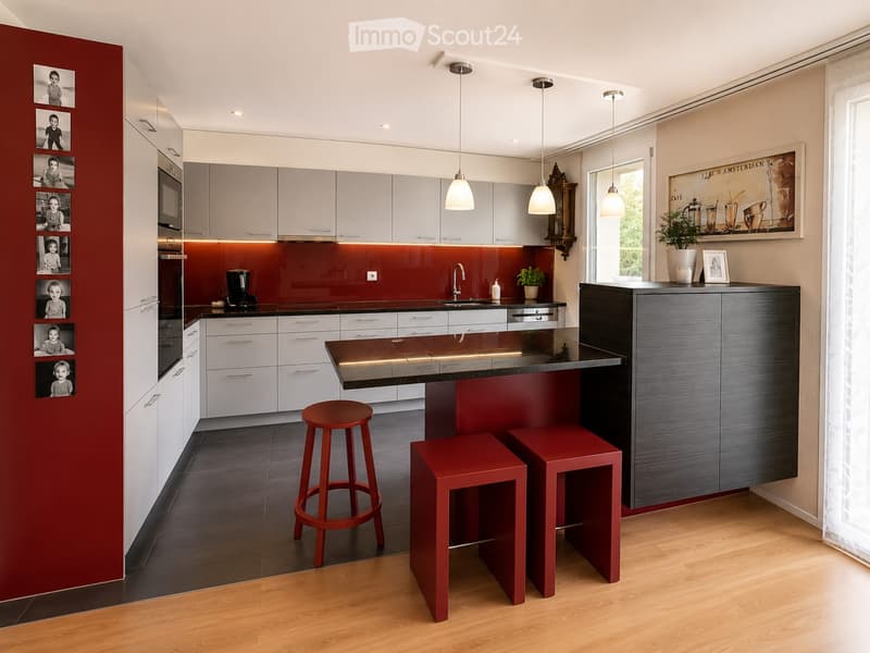 Modern kitchen with white cabinets, red accent wall, central island, and pendant lights. Includes stools, sink, coffee maker, and framed pictures.