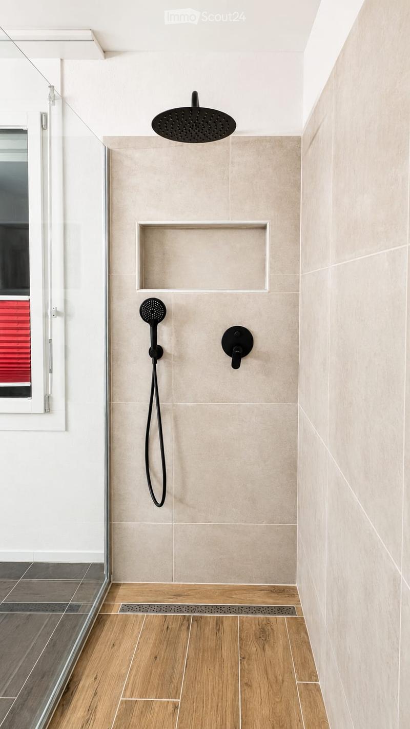 Modern shower area with a large overhead showerhead, handheld shower attachment, built-in shelf, and wooden flooring.