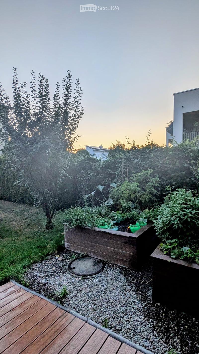 A small garden area with wooden planters, gravel ground cover, and surrounding greenery, including shrubs and trees.