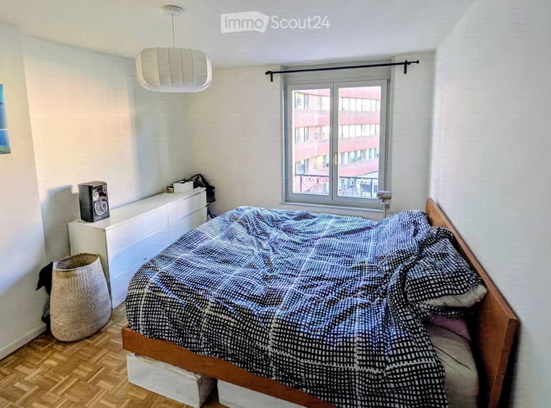 Cozy bedroom with a wooden bed, patterned duvet, nightstand with lamp, and a woven basket on the floor.