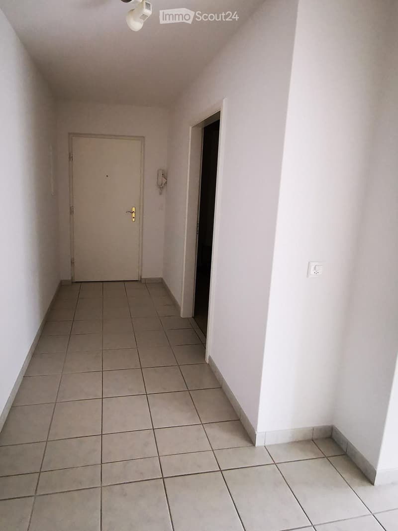 Empty hallway with tiled floor, white walls, and two doors, one closed and one open.