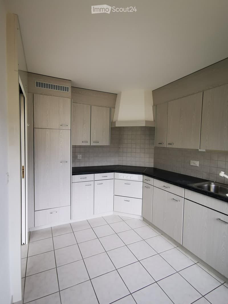 Modern kitchen with white tiled floor, light wood cabinets, black countertops, and stainless steel sink.