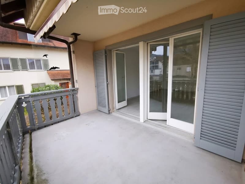 Balcony with grey railing, glass doors leading inside, and a view of neighboring buildings.