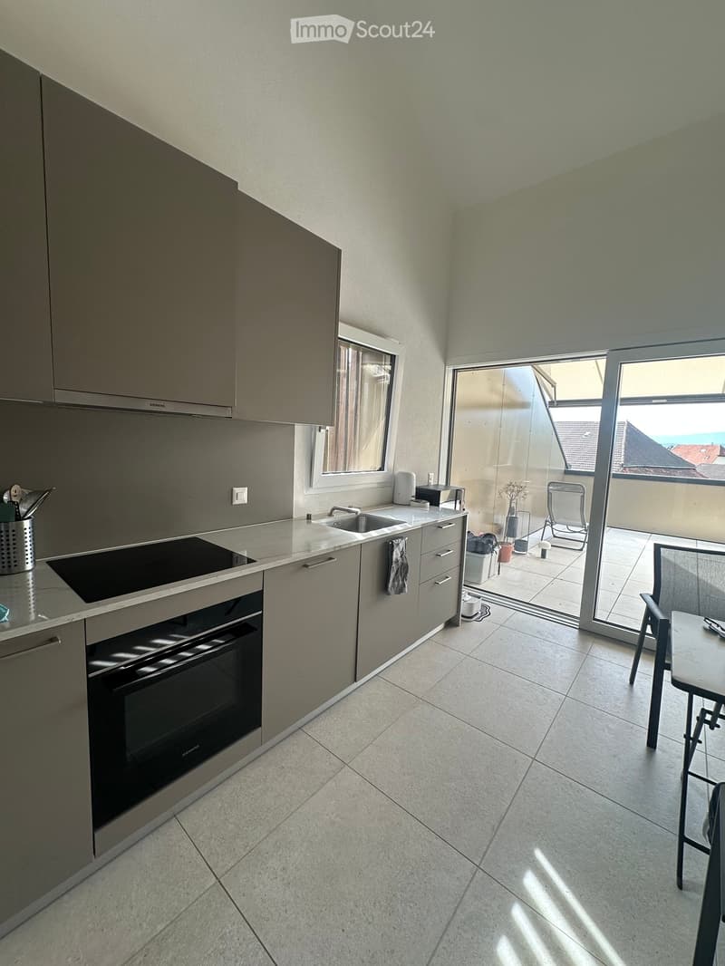 Modern kitchen with grey cabinets, stainless steel appliances, and a balcony with outdoor seating.