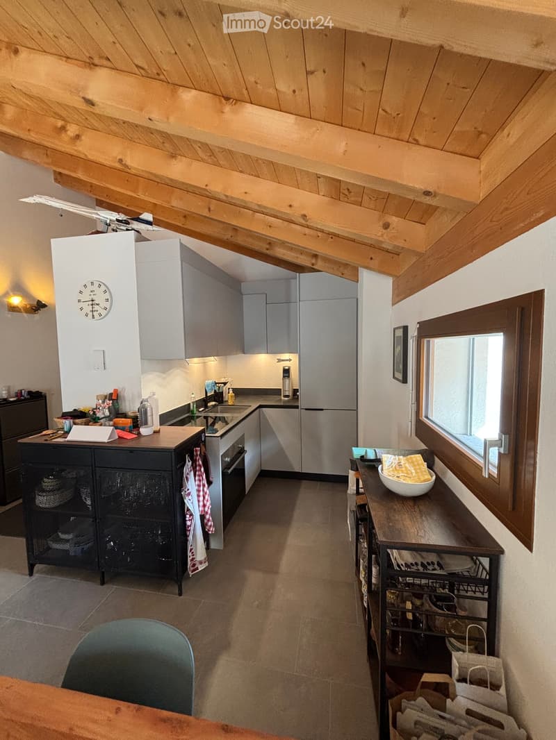 Modern kitchen with wooden beams, stainless steel appliances, and a mix of wooden and metal furniture.