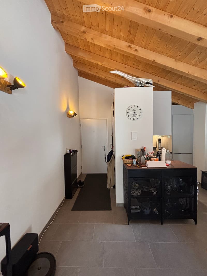 Hallway with wooden slanted ceiling, tiled floor, wall-mounted lighting, small cabinet, and a door leading to another room.
