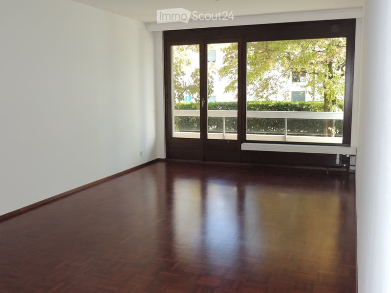 Empty room with polished wooden flooring, white walls, and large sliding glass doors leading to a balcony.