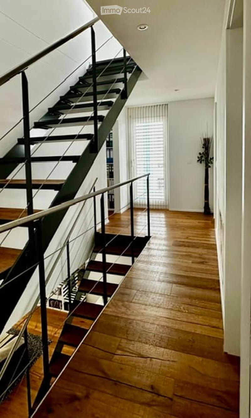 Modern hallway with wooden flooring, a staircase with black railings, and a tall window with blinds.