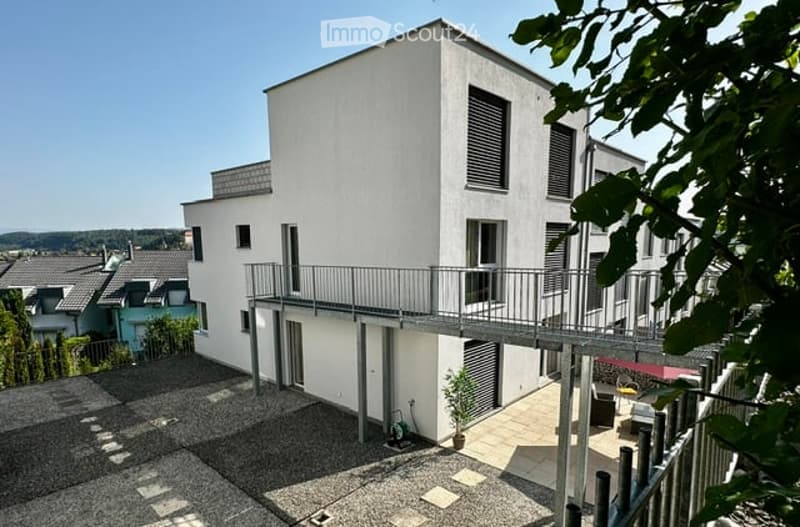 Modern two-story white building with a balcony and outdoor seating area.