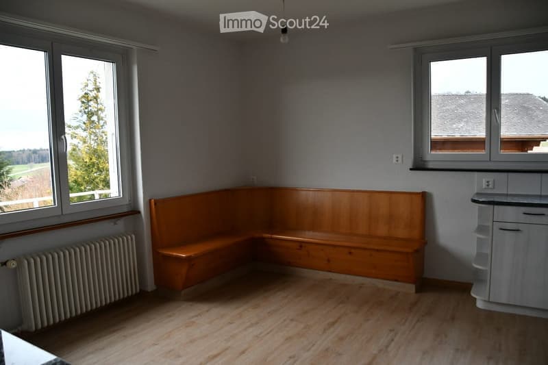 Empty room with wooden floor, built-in wooden bench seating, radiator, and small cabinet.