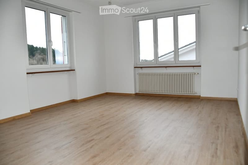 Empty room with light wooden flooring, white walls, and large windows offering a scenic view. No furniture or equipment present.