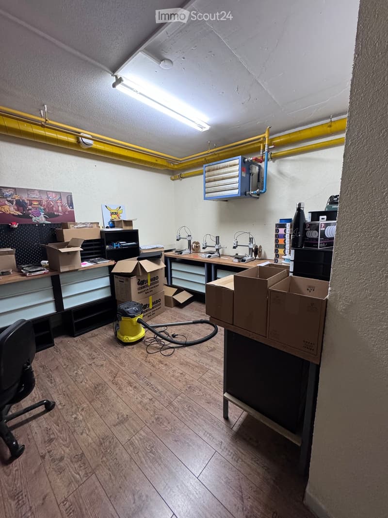 Workshop or studio space with wooden flooring, a chair, a table with tools, shelves, and several cardboard boxes.