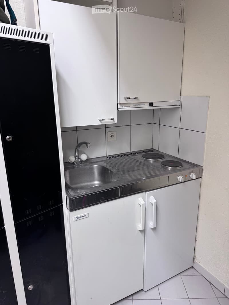 Compact kitchen with white cabinets, a stainless steel sink, a small electric stove, and a refrigerator.