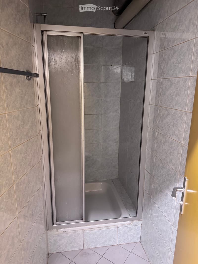 Modern bathroom with a glass-enclosed shower stall featuring grey tiles and a white frame. The shower stall has a sleek, contemporary design with a glass door and a visible interior space.