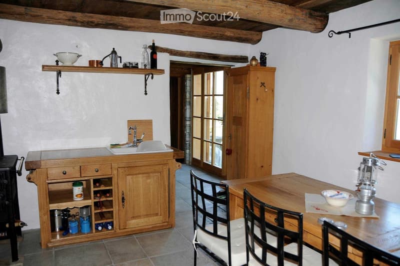 Cozy kitchen with wooden beams, sink, wooden cabinet, wine rack, table, chairs, and various kitchen items on shelves.