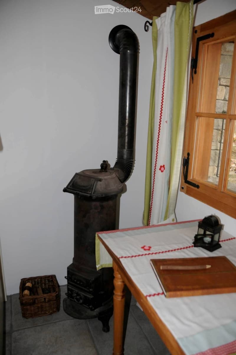 A rustic room with a wooden table, wooden cutting board, wooden stool, wooden window frame, wooden door, wooden basket, wooden lantern, wooden chair, and a wooden stove.