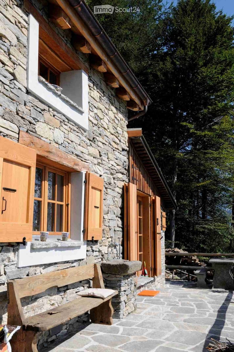 Stone house exterior with wooden shutters, stone bench, and outdoor seating area with a table and chairs.