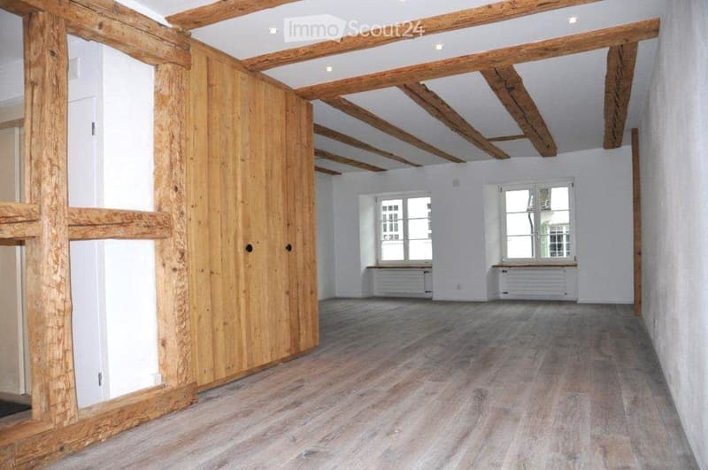 wooden floor, wooden beams, wooden walls, white walls, two windows, radiators, wooden door