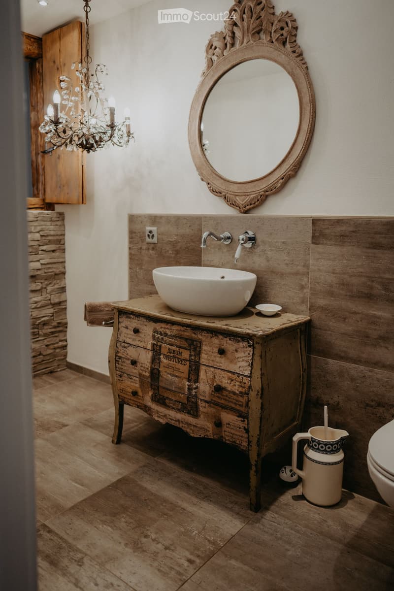bathroom with wooden vanity, sink, mirror, chandelier, stone pillar, toilet