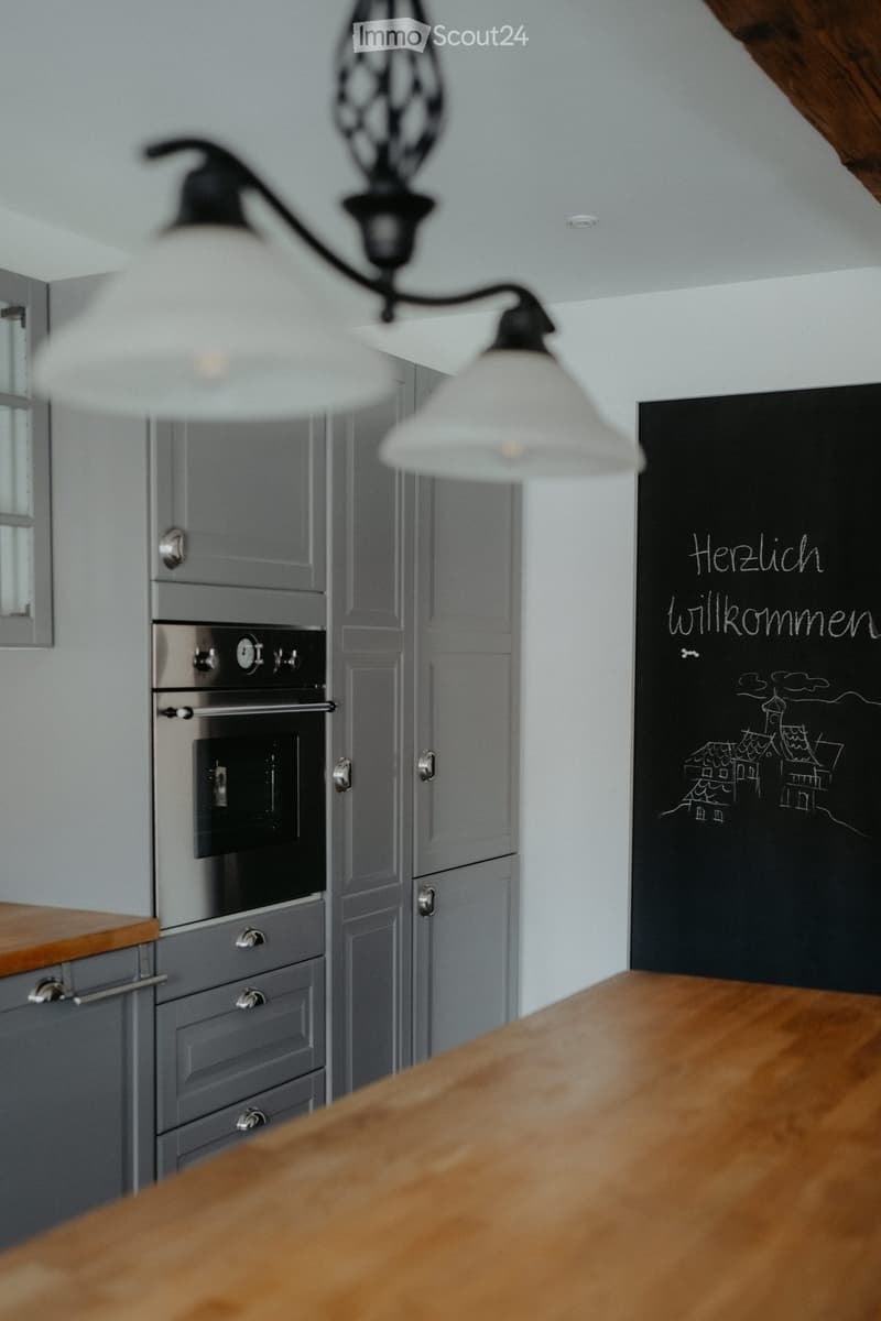wooden countertop, overhead lighting fixture, gray cabinetry, stainless steel oven, chalkboard with writing