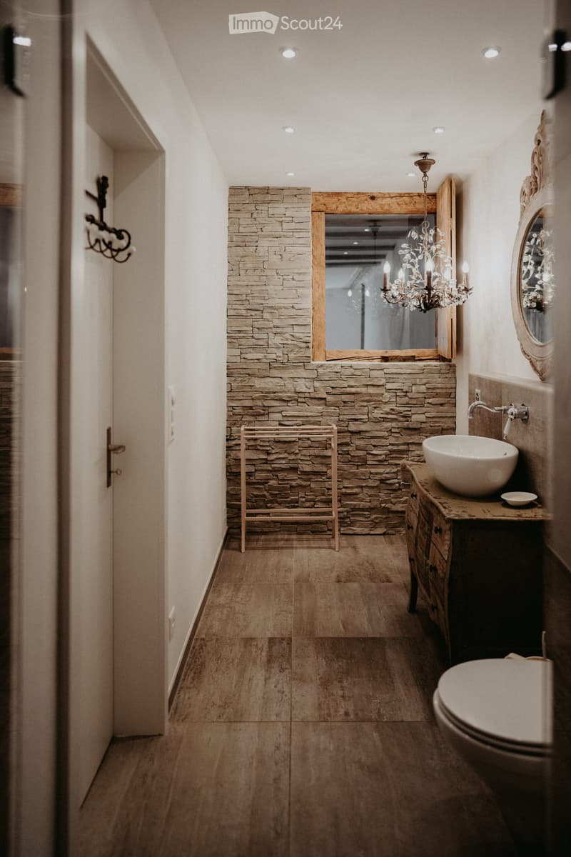 Bathroom with stone wall, chandelier, white sink, and toilet.