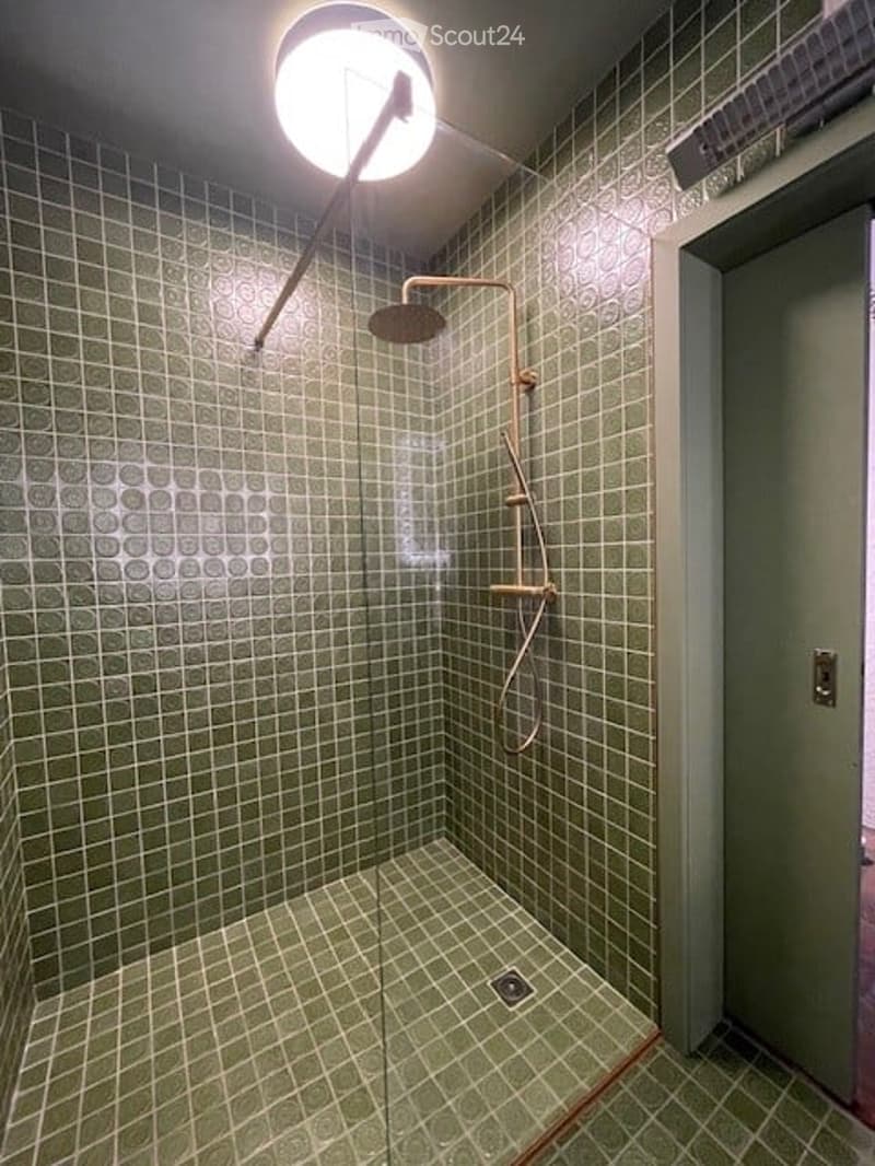 A glass enclosed shower with green tiles and a ceiling mounted light