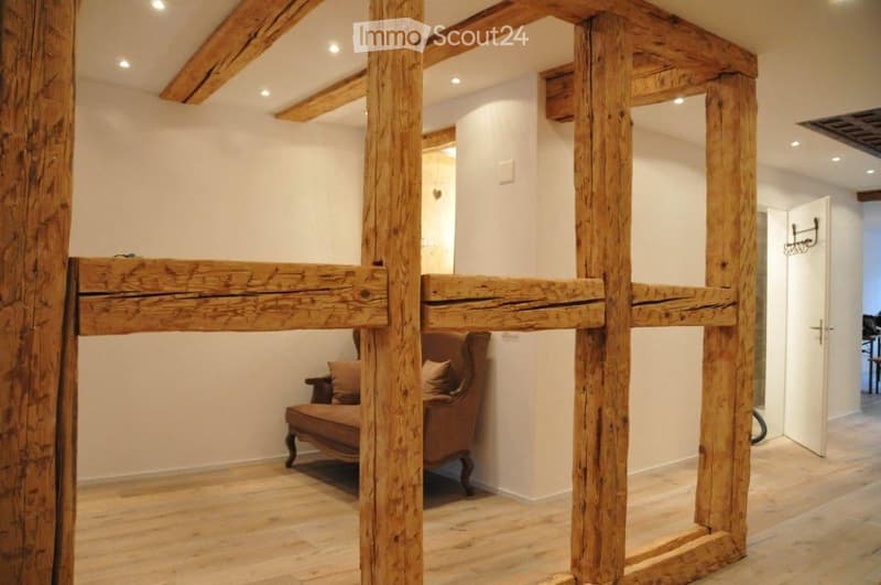 wooden beams, wooden floor, armchair with pillows, open door, white walls