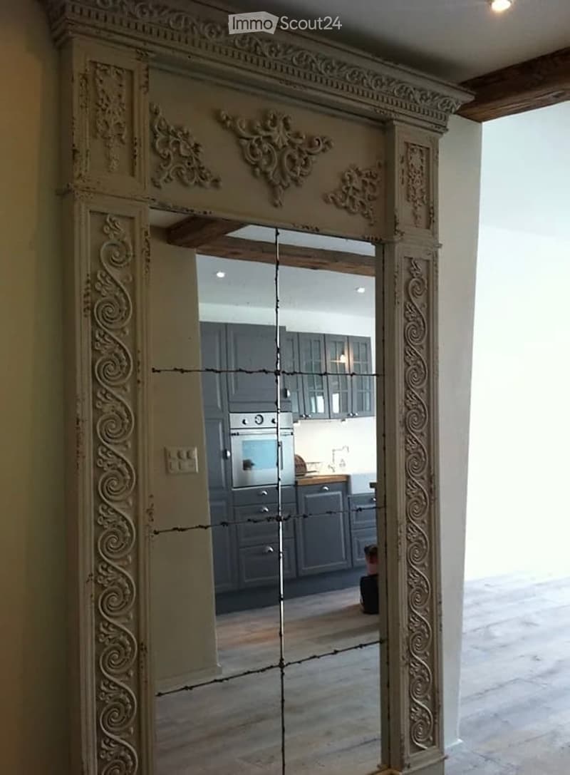 An ornate mirror is mounted on the wall, reflecting a room with gray cabinets, a microwave, and a gas stove.