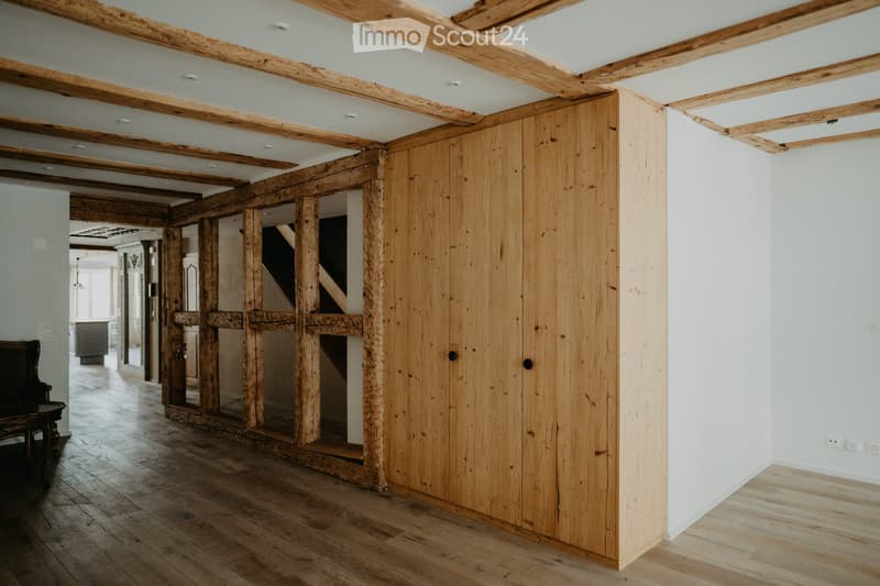 wooden floors, wooden beams, wooden paneling, white walls, open doorway, small table, armchair