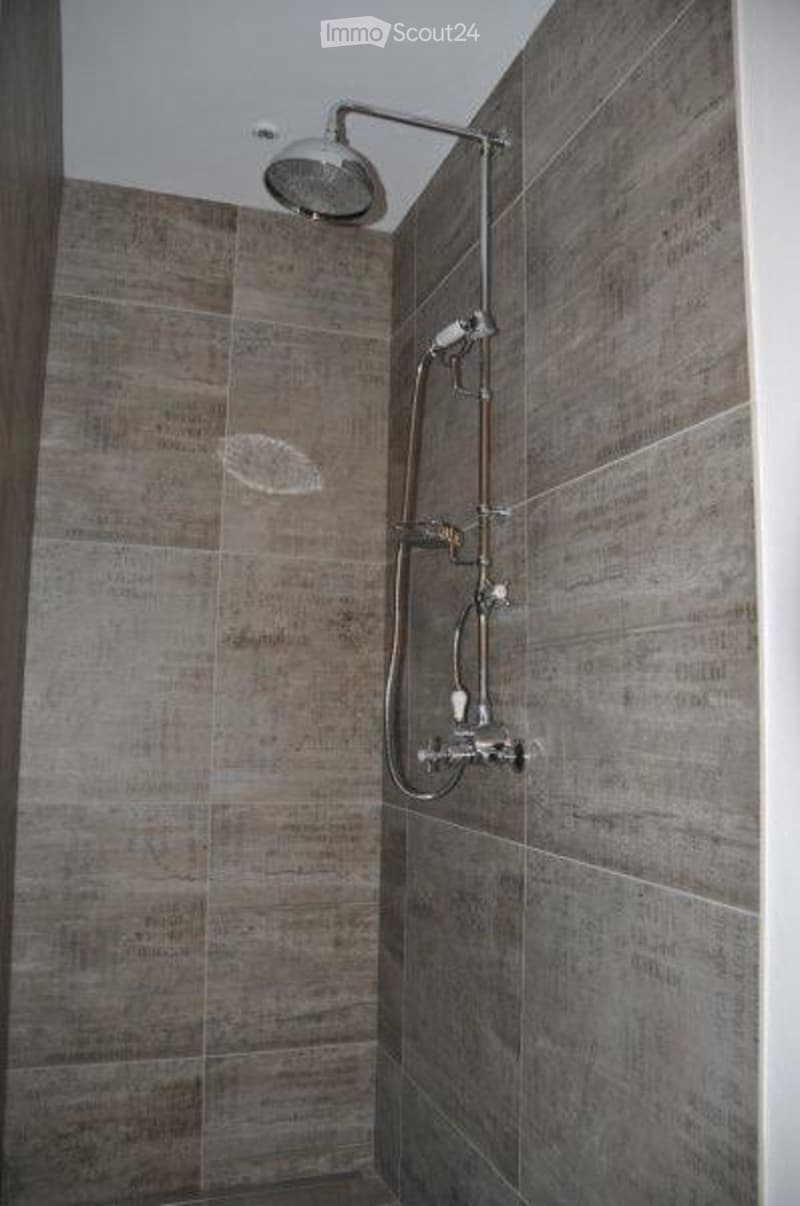 grey tiled shower with a shower head and a hose with a fixed spray