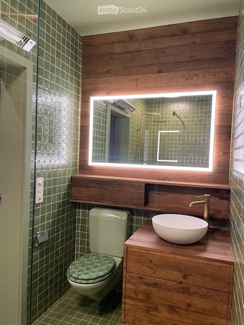 Green tiles, toilet, sink, mirror, brass faucet, wooden cabinet