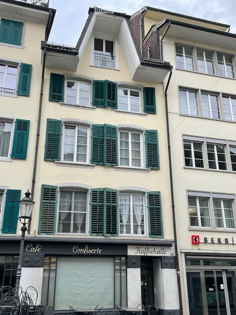 Apartment building with green shutters, balcony on second floor, cafe at ground floor