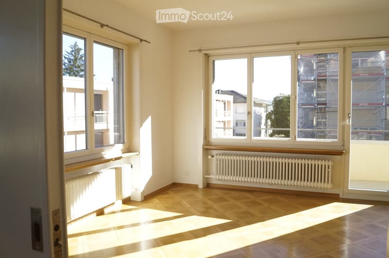 Empty room with wooden flooring, large windows, radiators, and natural light streaming in.