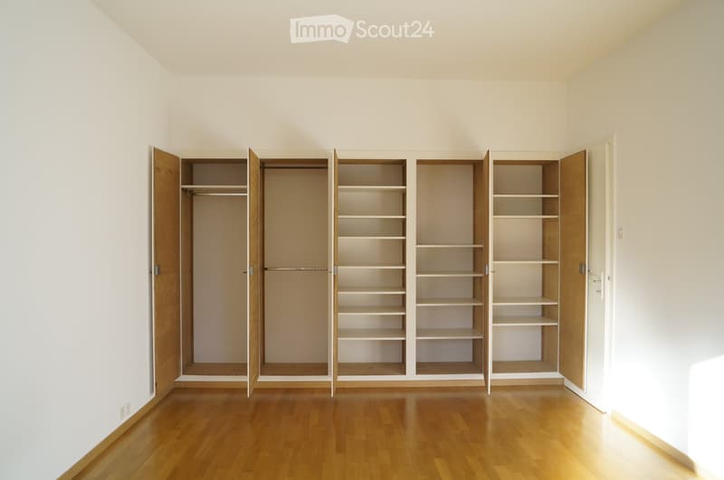 Empty room with wooden flooring and built-in wooden closet units with open shelves and hanging space.